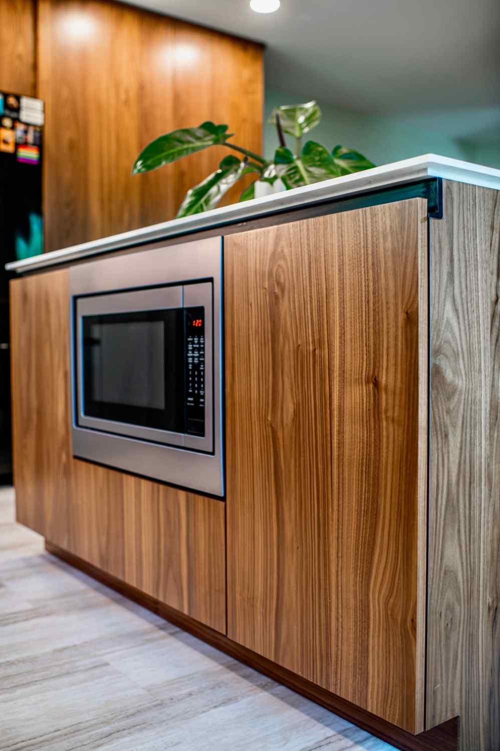 Walnut kitchen island with an integrated microwave, waterfall countertop edge and full-height walnut cabinetry behind